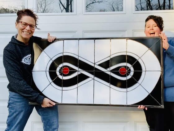 Monica and Candace holding a stained glass window of the Snowy Owl Coffee logo