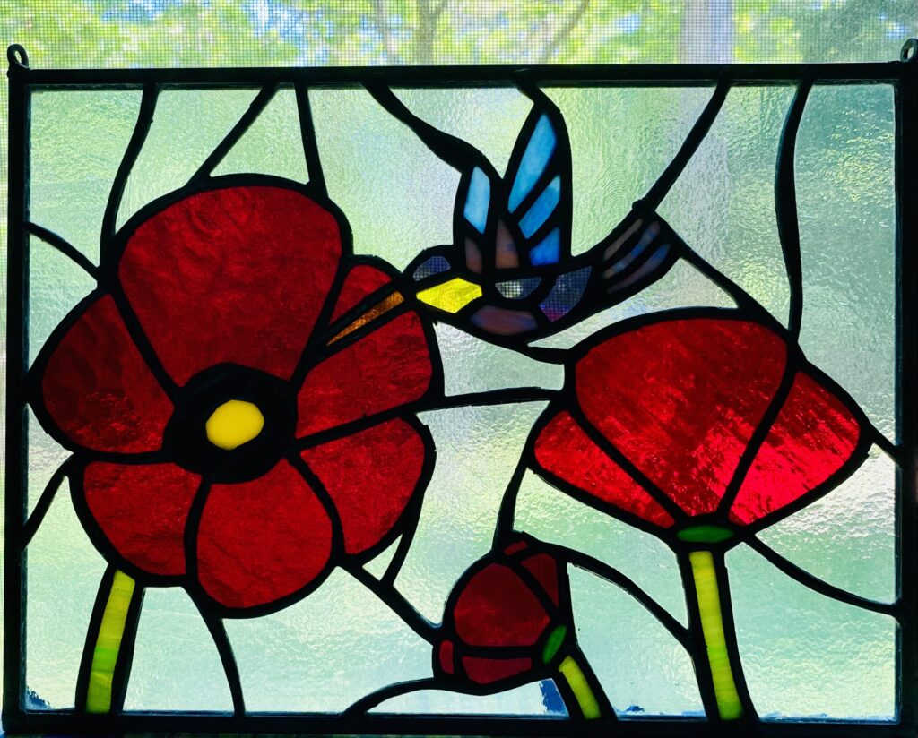 stained glass window of a hummingbird flying toward a poppy.