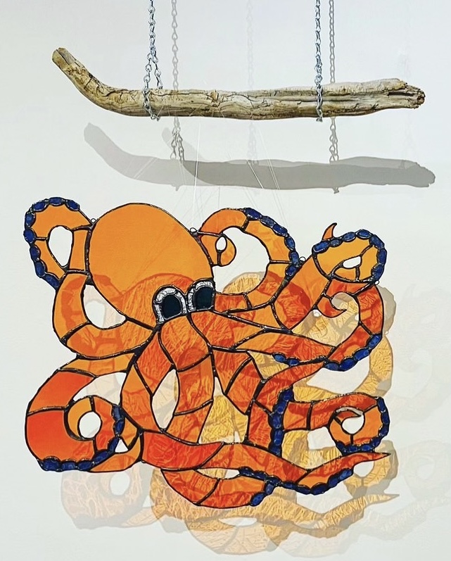 An orange stained-glass octopus hangs from a piece of drift wood.
